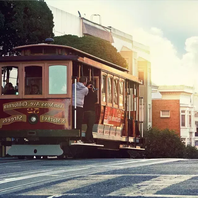 Un téléphérique contourne une colline à San Francisco avec des passagers regardant par la fenêtre.